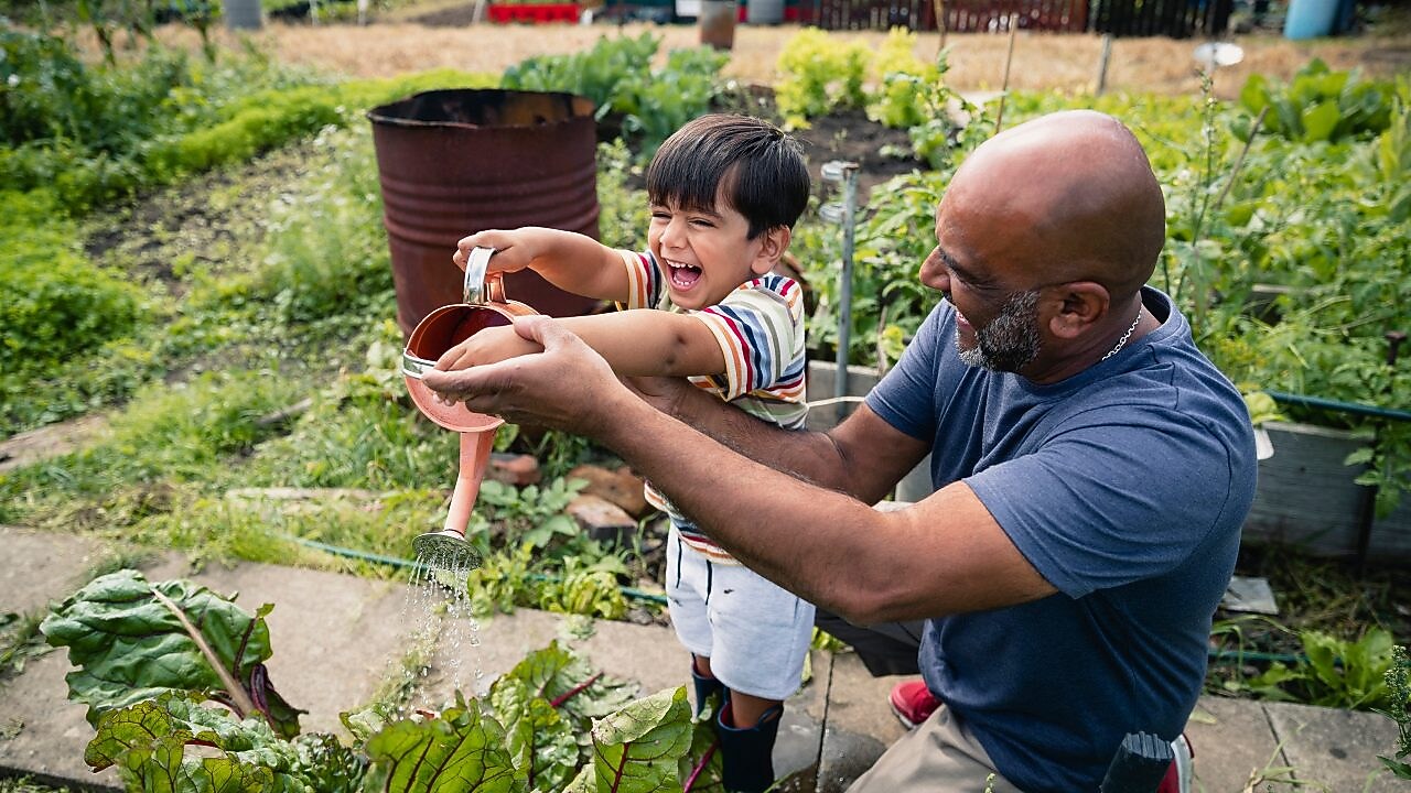 Hombre ayudando a un niño sonriente a regar las plantas en un jardín
