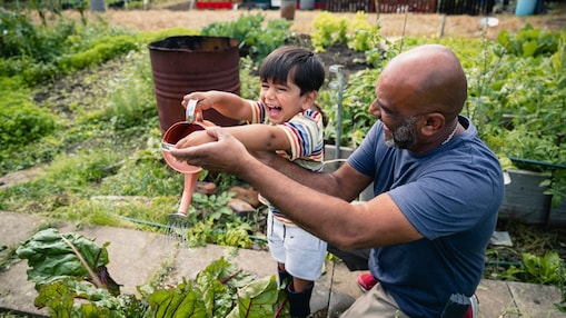 Hombre ayudando a un niño sonriente a regar las plantas en un jardín