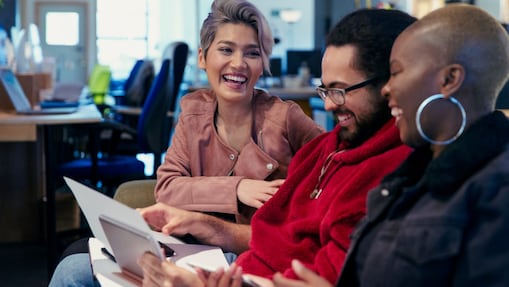 Tres personas en una oficina sentados juntos, mirando papeles y riendo