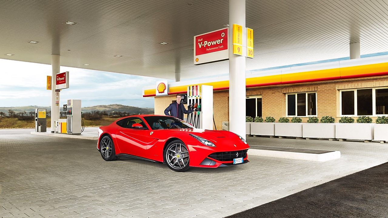 Ferrari rojo en una estación de servicio Shell con un hombre apoyado sobre un surtidor