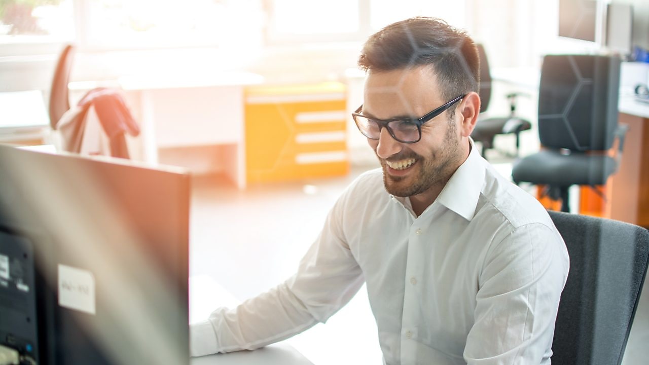 Hombre sonrie mirando a la pantalla de su computadora