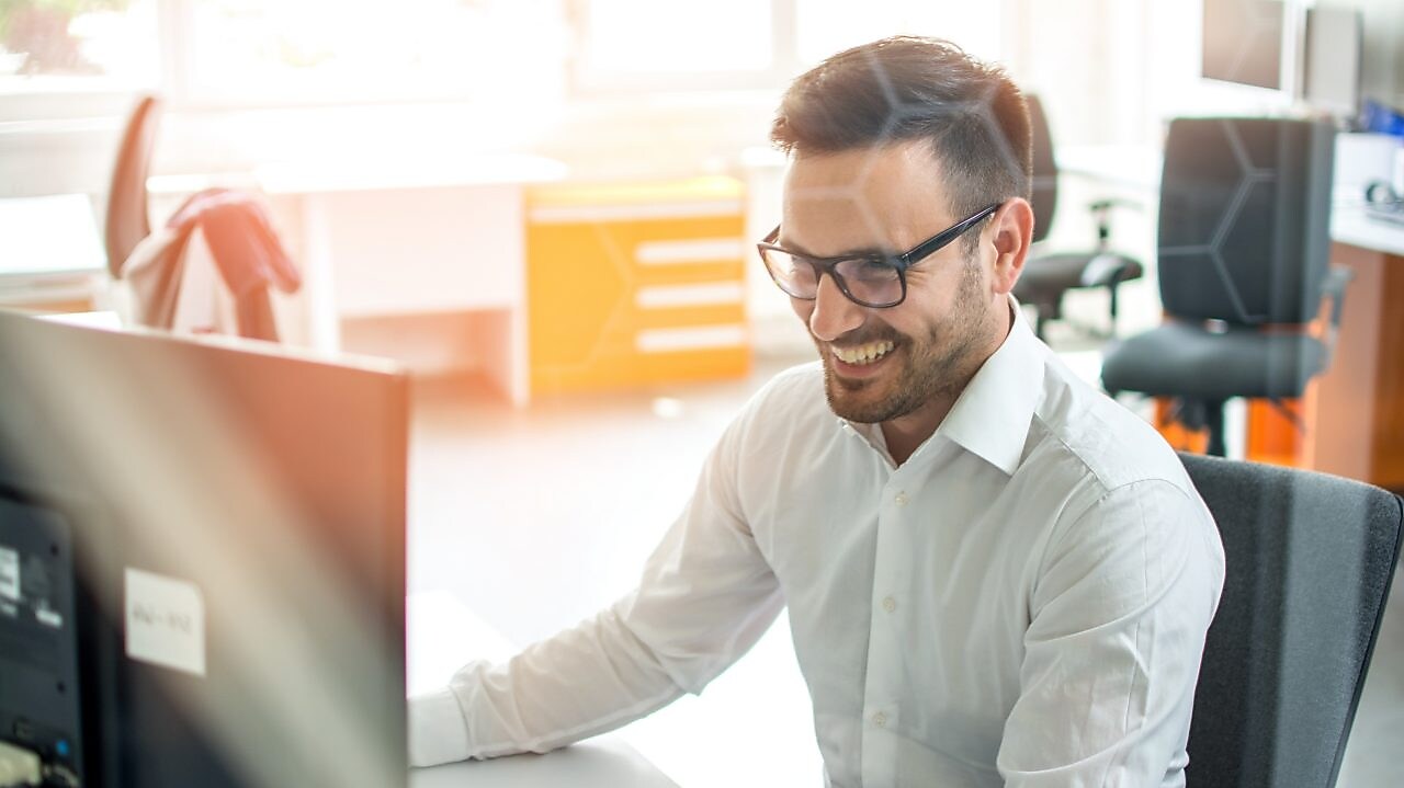Hombre sonrie mirando a la pantalla de su computadora