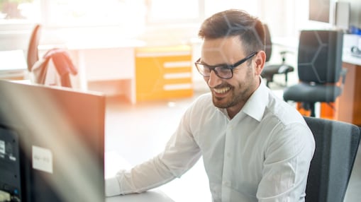 Hombre sonrie mirando a la pantalla de su computadora