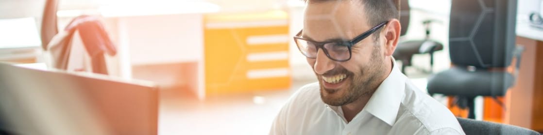 Hombre sonrie mirando a la pantalla de su computadora